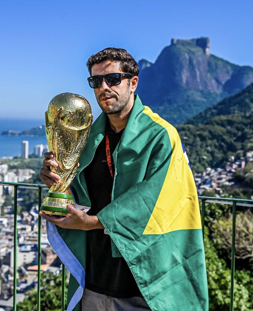 Lucas Vallejos com a bandeira do Brasil e a taça, com a Pedra da Gávea ao fundo